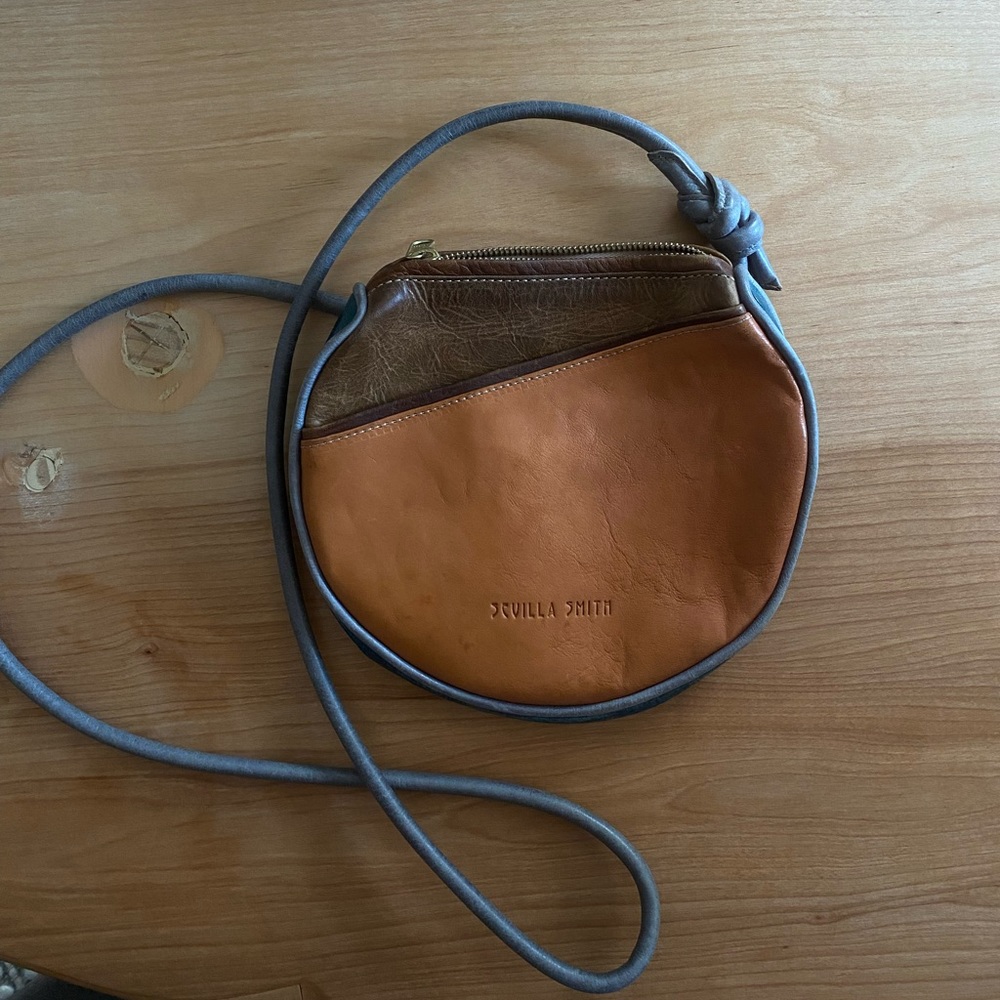 Small leather bag with an open pocket on the front and adjustable strap.